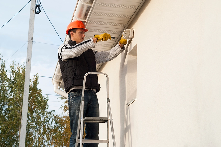 Electrician, heeding electrical installation safety guidelines, installing outdoor lighting on the home of a Springfield, IL resident.)